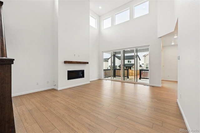 unfurnished living room featuring light wood finished floors, baseboards, a glass covered fireplace, and a high ceiling
