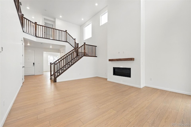 unfurnished living room featuring stairway, a towering ceiling, light wood-type flooring, baseboards, and a glass covered fireplace