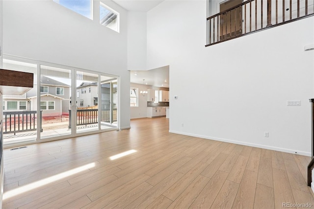 unfurnished living room featuring wood finished floors, a wealth of natural light, baseboards, and visible vents
