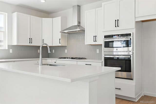 kitchen featuring stainless steel double oven, a sink, gas cooktop, wall chimney exhaust hood, and white cabinetry