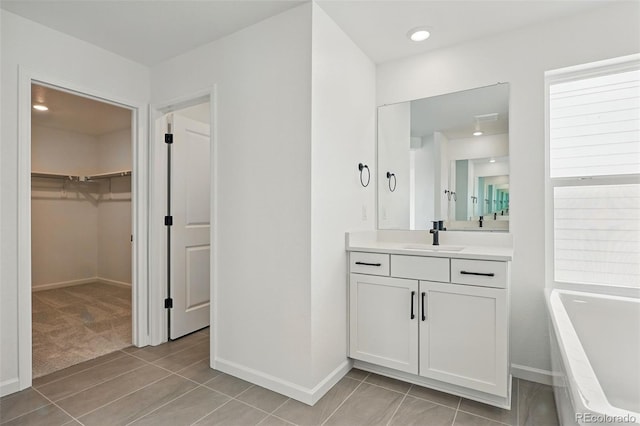 full bathroom featuring tile patterned floors, a spacious closet, vanity, a tub, and baseboards