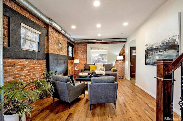 living room with light wood-type flooring, plenty of natural light, brick wall, and stairway