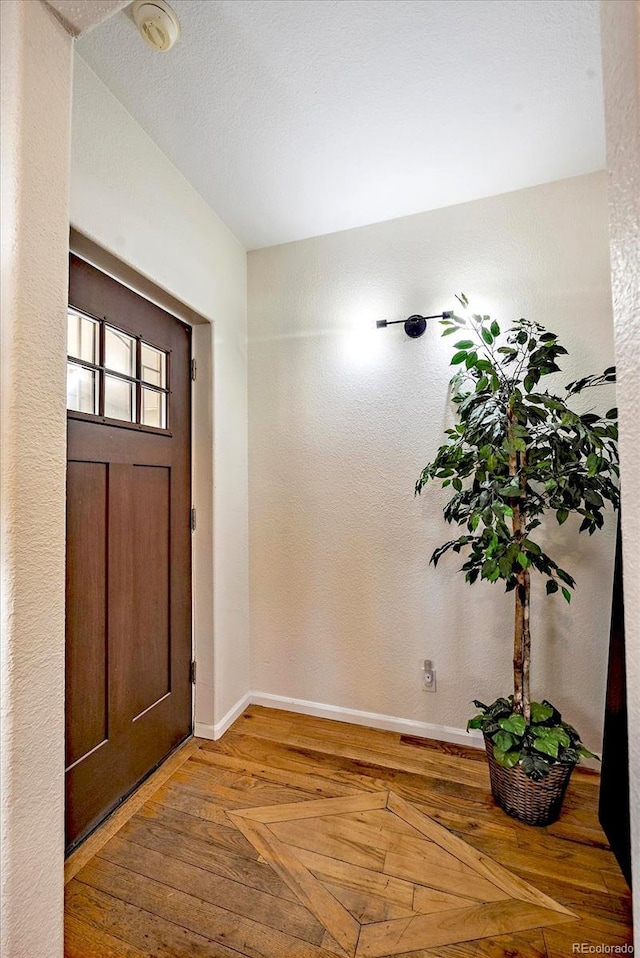 foyer entrance featuring a textured wall, baseboards, and wood finished floors