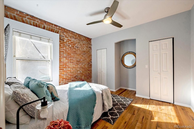 bedroom with wood finished floors, baseboards, brick wall, ceiling fan, and multiple closets