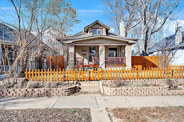 bungalow-style home with a porch, a fenced front yard, and a shingled roof