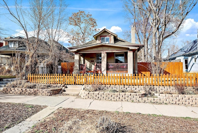 bungalow with a fenced front yard, covered porch, and a chimney