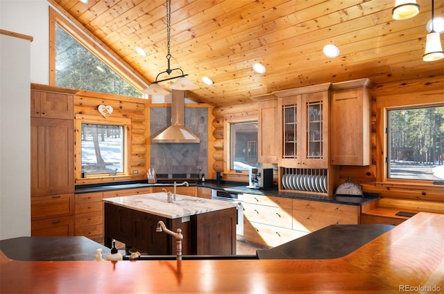 kitchen featuring glass insert cabinets, wall chimney range hood, wood ceiling, an island with sink, and rustic walls