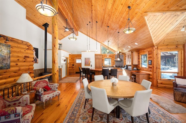 dining room with light wood finished floors, wooden ceiling, high vaulted ceiling, and a wood stove