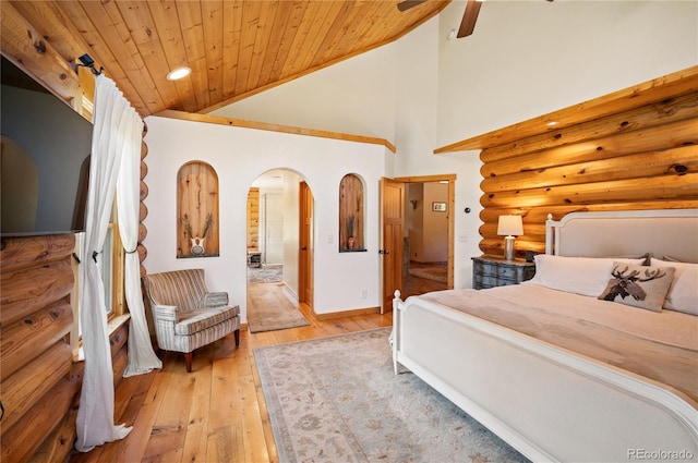 bedroom featuring light wood-style flooring, wooden ceiling, arched walkways, rustic walls, and high vaulted ceiling