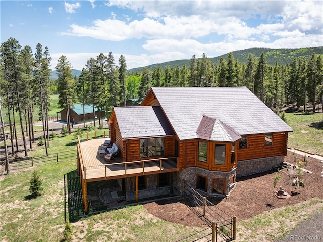 exterior space featuring a deck with mountain view, fence, a view of trees, and stone siding