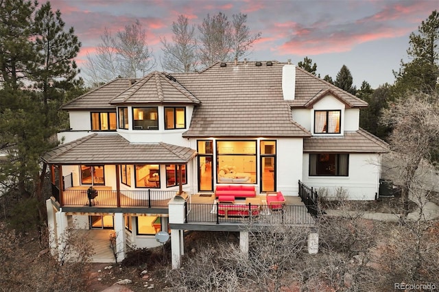 back of house at dusk featuring a patio area, a chimney, an outdoor hangout area, and stucco siding