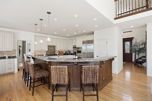 kitchen with stainless steel appliances, light wood-style flooring, a kitchen bar, and a large island with sink