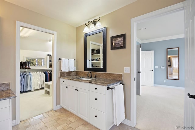 full bath with a walk in closet, stone tile flooring, ornamental molding, vanity, and baseboards