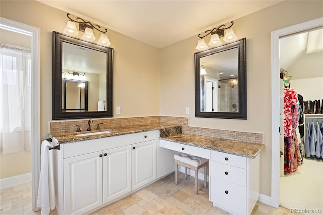 bathroom with a walk in closet, tasteful backsplash, stone finish floor, vanity, and baseboards