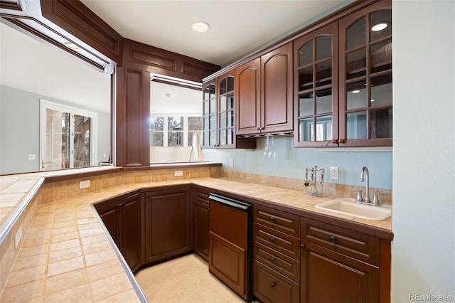 kitchen with tile countertops, recessed lighting, glass insert cabinets, a sink, and a peninsula