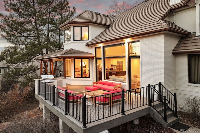 rear view of property featuring a tile roof, brick siding, an outdoor kitchen, and an outdoor hangout area