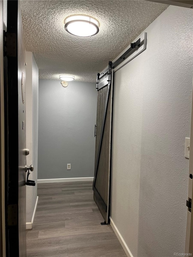 hall with a barn door, hardwood / wood-style floors, and a textured ceiling