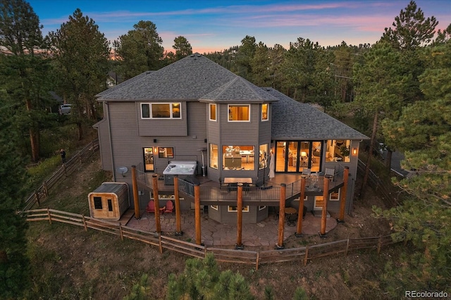 back of property at dusk featuring a shingled roof, fence, and a deck