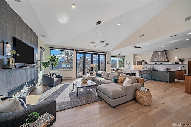 living room with a large fireplace, visible vents, light wood finished floors, and high vaulted ceiling