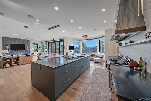 kitchen featuring a spacious island, wall chimney exhaust hood, modern cabinets, open floor plan, and a sink