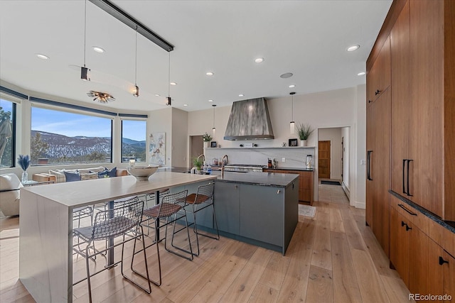 kitchen with wall chimney range hood, modern cabinets, light wood-style flooring, and brown cabinets