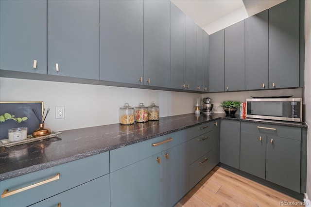 kitchen with dark stone counters, stainless steel microwave, and light wood-type flooring