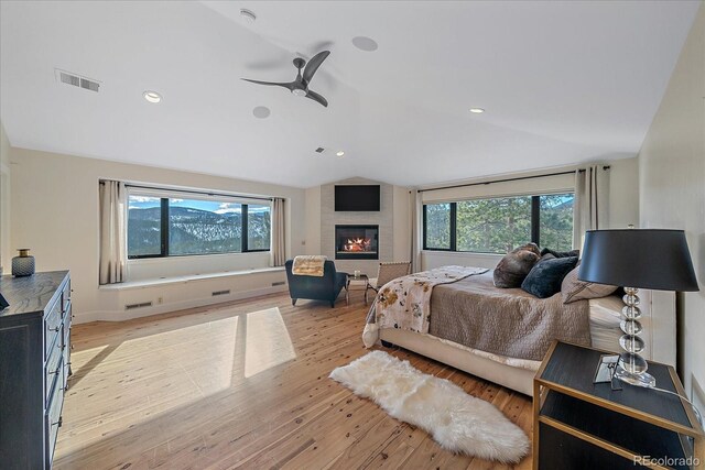 bedroom featuring a large fireplace, visible vents, vaulted ceiling, and light wood finished floors