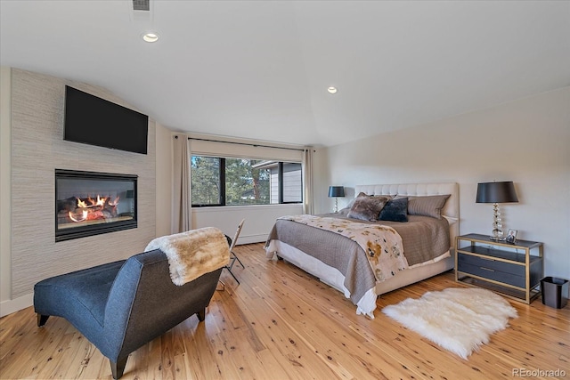 bedroom featuring recessed lighting, vaulted ceiling, hardwood / wood-style floors, and a glass covered fireplace