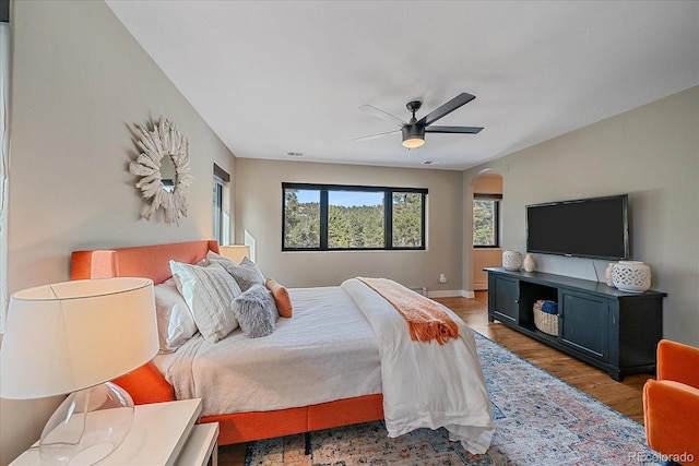 bedroom with arched walkways, multiple windows, wood finished floors, and a ceiling fan