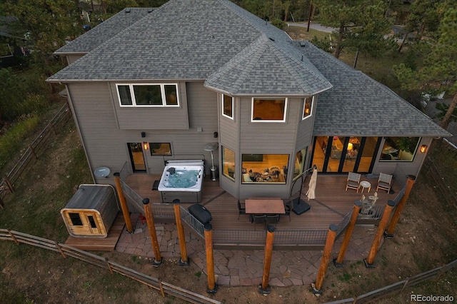 rear view of house featuring a deck, roof with shingles, fence, and a hot tub