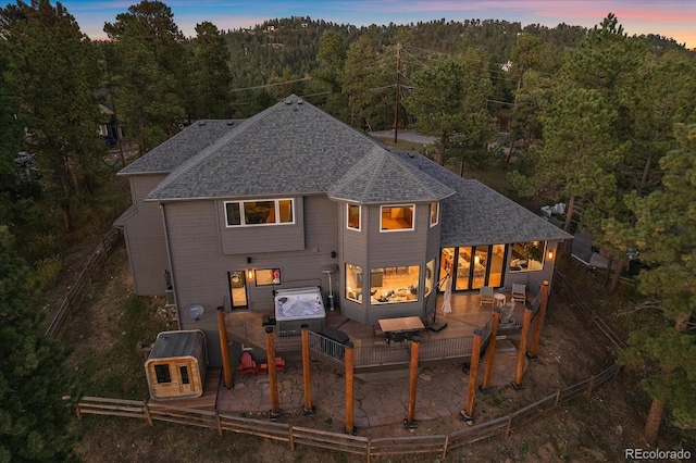 rear view of house with a deck, a shingled roof, and a wooded view