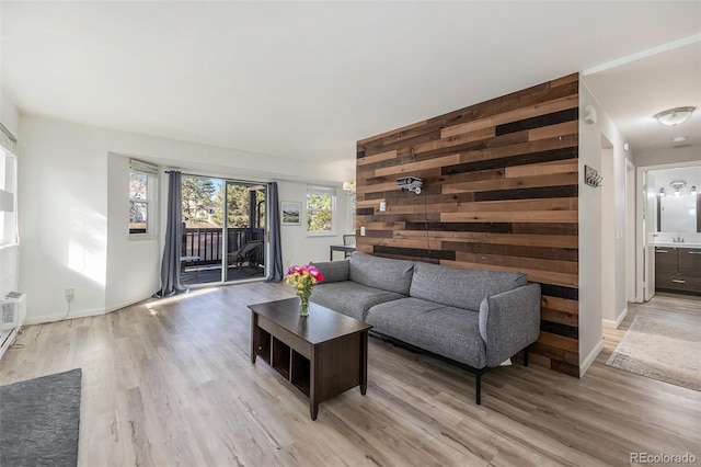 living area featuring baseboards, wood walls, an accent wall, and light wood finished floors