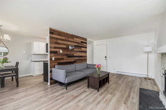 living area featuring a baseboard heating unit, baseboards, a notable chandelier, and light wood-style flooring