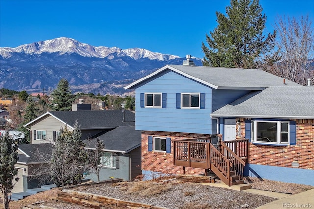 tri-level home with brick siding, a deck with mountain view, and a shingled roof