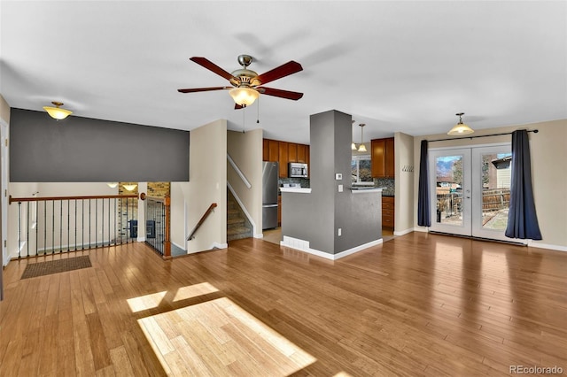 unfurnished living room featuring baseboards, stairs, french doors, light wood-style floors, and a ceiling fan