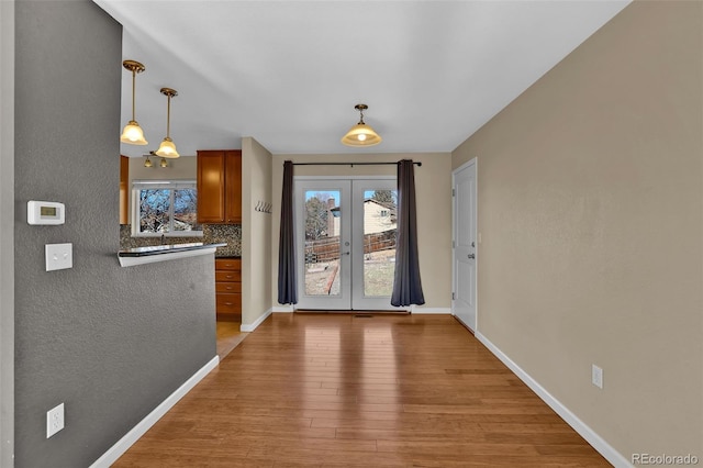 interior space with baseboards, french doors, light wood-style floors, and a healthy amount of sunlight