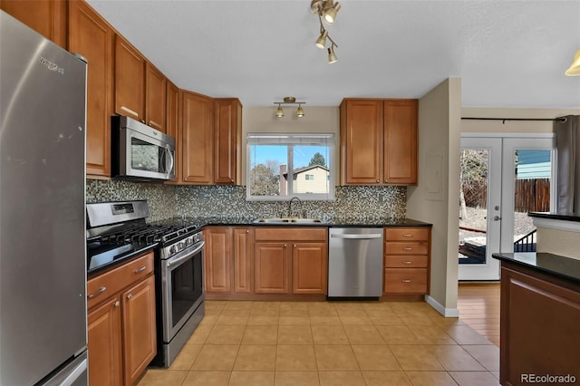 kitchen with brown cabinets, a sink, dark countertops, tasteful backsplash, and stainless steel appliances