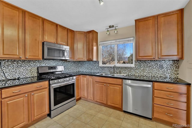 kitchen featuring brown cabinets, a sink, backsplash, appliances with stainless steel finishes, and light tile patterned floors