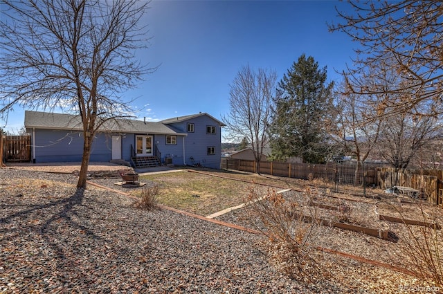 back of house with entry steps, french doors, a fenced backyard, and roof with shingles