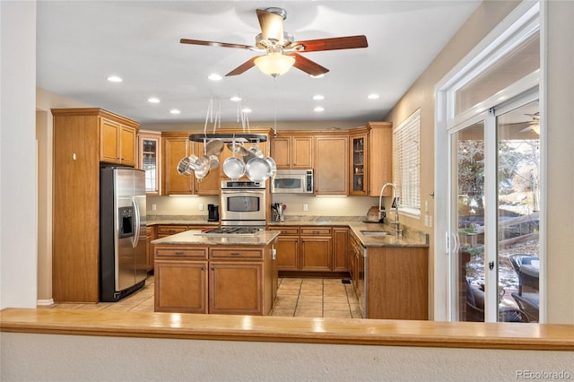 kitchen with light stone countertops, stainless steel appliances, ceiling fan, sink, and a kitchen island