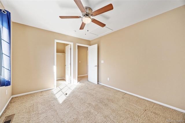 unfurnished bedroom featuring a walk in closet, light colored carpet, and ceiling fan