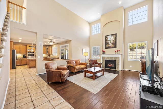 living room featuring ceiling fan, light wood-type flooring, sink, and a towering ceiling