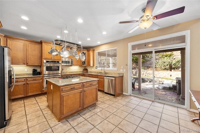 kitchen with ceiling fan, sink, a center island, light stone counters, and appliances with stainless steel finishes