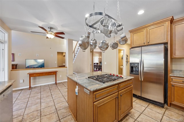 kitchen with ceiling fan, a kitchen island, light stone countertops, and stainless steel appliances