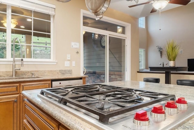 6987 Esperanza Dr, Castle Pines, CO 80108 - kitchen featuring stainless steel gas stovetop, a sink, brown cabinets, and light stone counters