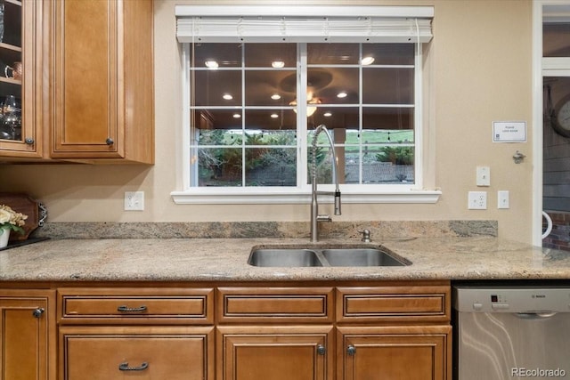 6987 Esperanza Dr, Castle Pines, CO 80108 - kitchen featuring stainless steel dishwasher, brown cabinets, a sink, glass insert cabinets, and light stone countertops