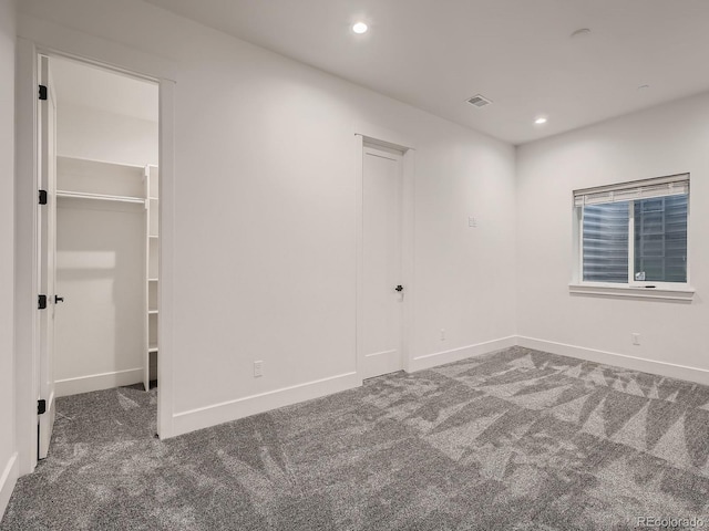 unfurnished bedroom with a spacious closet, dark colored carpet, and a closet