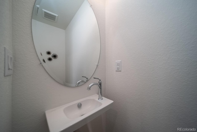 bathroom featuring visible vents, a textured wall, and a sink