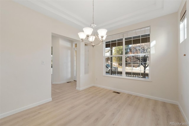 unfurnished dining area featuring a chandelier, light hardwood / wood-style floors, and a raised ceiling