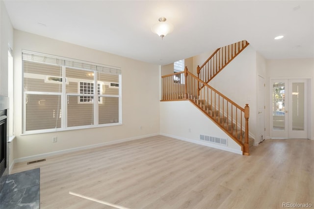 unfurnished living room featuring a fireplace, french doors, and light wood-type flooring